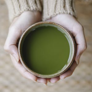 Top view of crop anonymous female showing bowl full of green tea of matcha in hands on blurred background